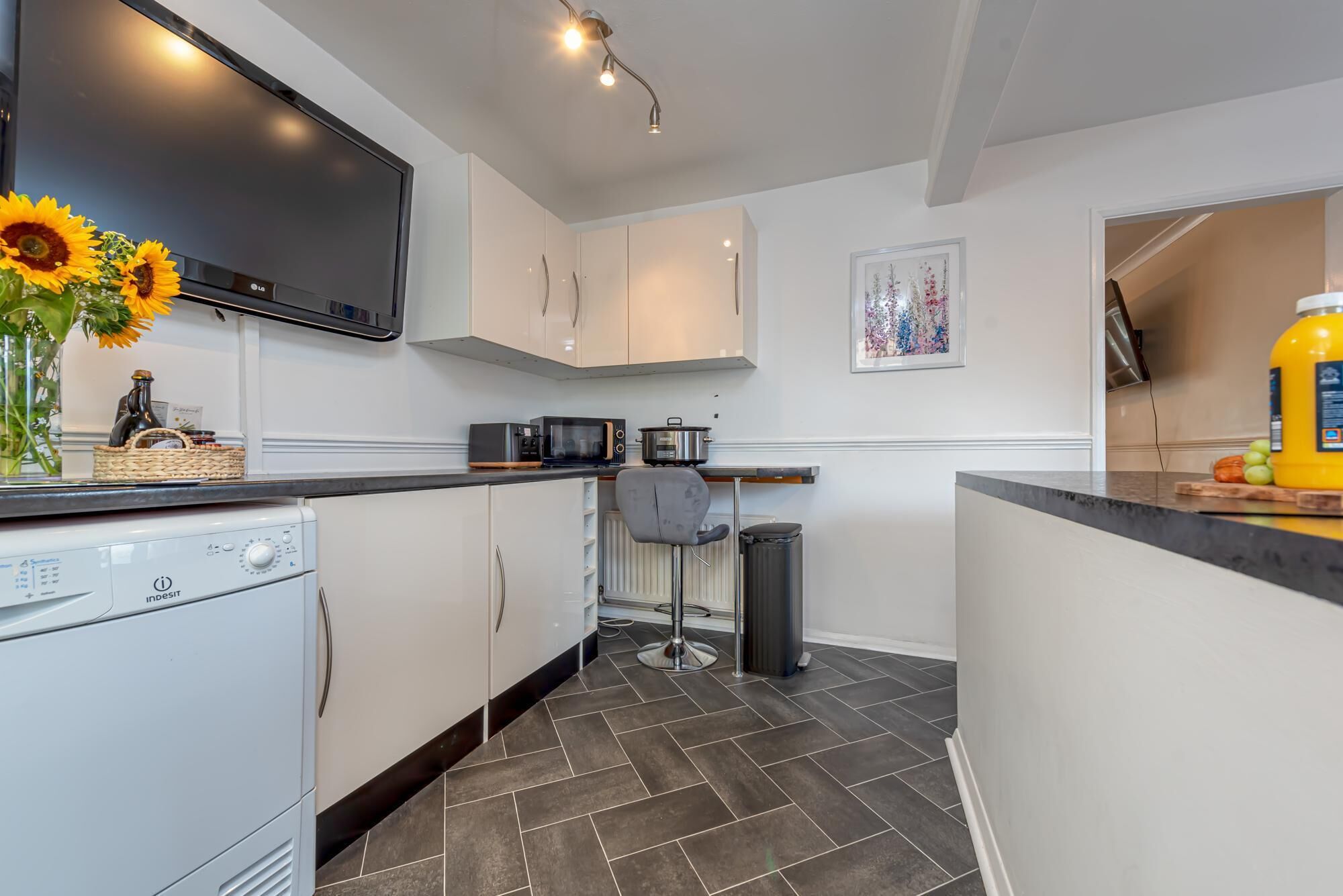 A modern kitchen with white cabinetry, a built-in microwave, and a large flat-screen TV.