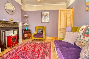 A room with a fireplace, a red cabinet, a patterned rug, a yellow armchair, and a purple sofa. - Large Family House close to Cathedral Quarter - Pass the Keys (Lincoln)