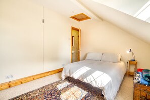 A bedroom with a sloped ceiling, a bed with a white bedspread, a nightstand with a lamp, and a patterned rug. - Large Family House close to Cathedral Quarter - Pass the Keys (Lincoln)