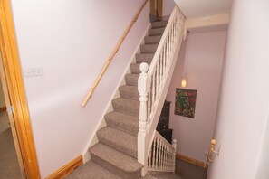 A staircase with a wooden handrail and white balusters, carpeted steps, and a wall-mounted light fixture. - Large Family House close to Cathedral Quarter - Pass the Keys (Lincoln)