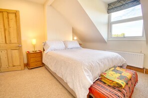 Un dormitorio con cama, mesita de noche, lámpara, ventana y radiador.