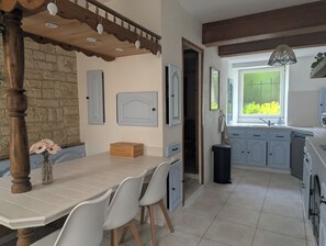 Un comedor con una mesa y sillas de madera, una pared de piedra y vista a la cocina.