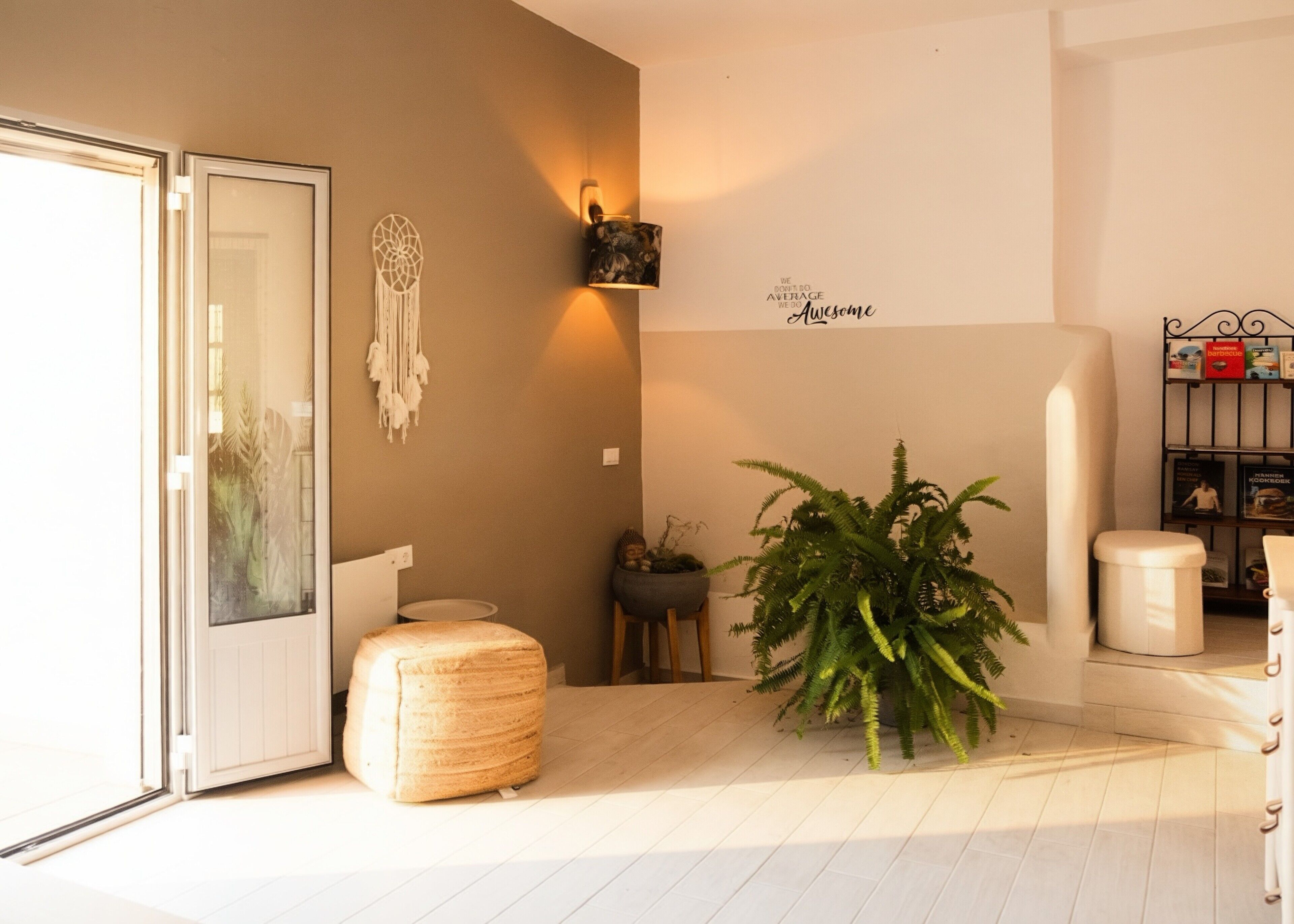 Un intérieur moderne avec une porte en verre, un pouf rond, un luminaire fixé au mur, une fougère en pot et une bibliothèque.