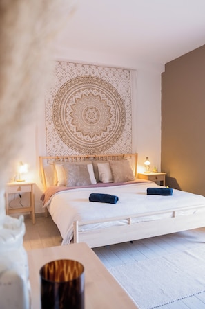 A bedroom with a bed, bedside tables, a wall tapestry, and a nightstand with a lamp.