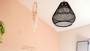 A bedroom with a bed, a bedside table, a hanging light fixture, and a wall with a dreamcatcher and a motivational quote.