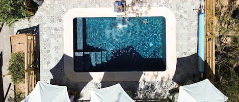 Una piscina con borde de azulejos, terraza de madera y sombrillas.