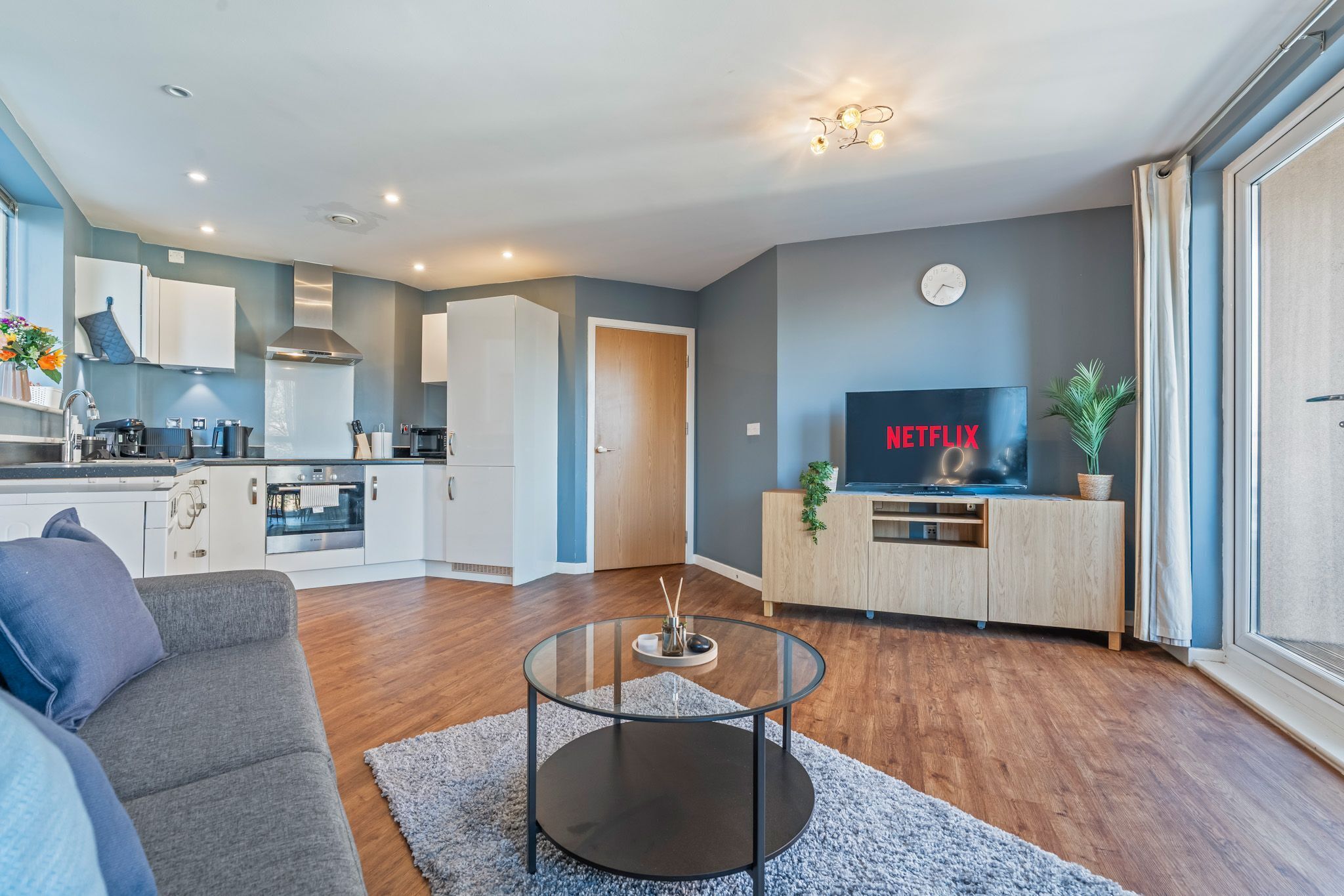 A modern apartment with a kitchen, living room, and a TV displaying 'NETFLIX'.