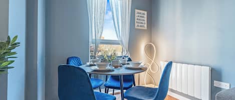 Un comedor con una mesa redonda, sillas azules y una ventana con cortinas traslúcidas.