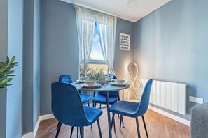 Ein Essbereich mit einem runden Tisch, blauen Stühlen und einem Fenster mit transparenten Vorhängen.