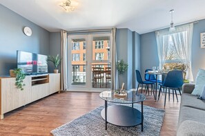 A modern living room with a TV, a glass coffee table, and a dining area with blue chairs. - Luxury Birmingham City Centre Stay + Free Parking (Birmingham)