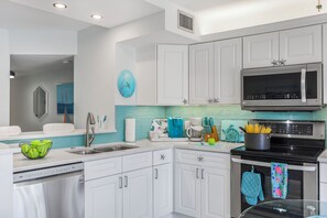 A modern kitchen with white cabinetry, a stainless steel dishwasher, a microwave, and a stove. - Riverfront condo | Olde Marco | pools & pickleball (Marco Island)