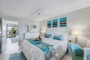 A bedroom with a bed, a ceiling fan, a nightstand, a lamp, and artwork on the wall. - Riverfront condo | Olde Marco | pools & pickleball (Marco Island)
