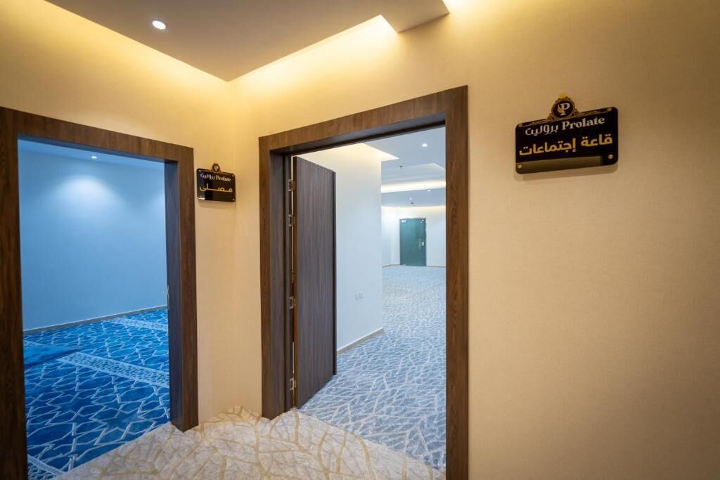 Un pasillo de hotel con un letrero que indica la habitación Prolata, un suelo con diseño y vista hacia la habitación contigua.