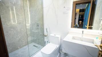 Un baño moderno con cabina de ducha de vidrio, inodoro blanco y lavamanos de mármol.