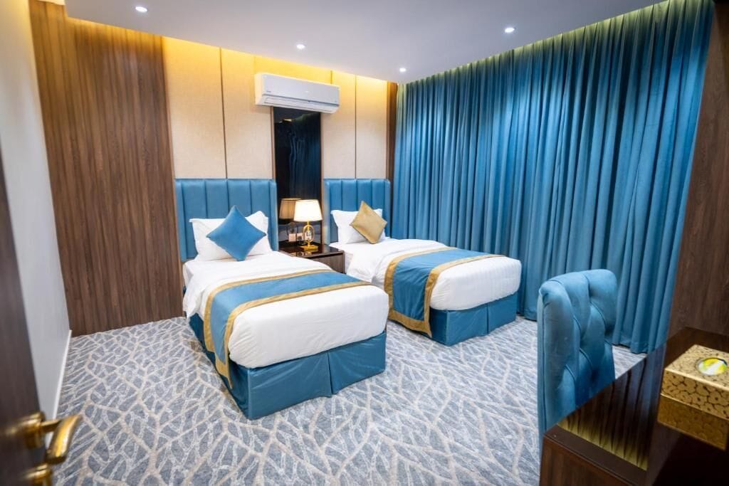 Una habitación de hotel con dos camas, una mesita de noche, una lámpara y una silla azul.