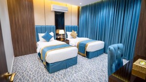 Una habitación de hotel con dos camas, una mesita de noche, una lámpara y una silla azul.