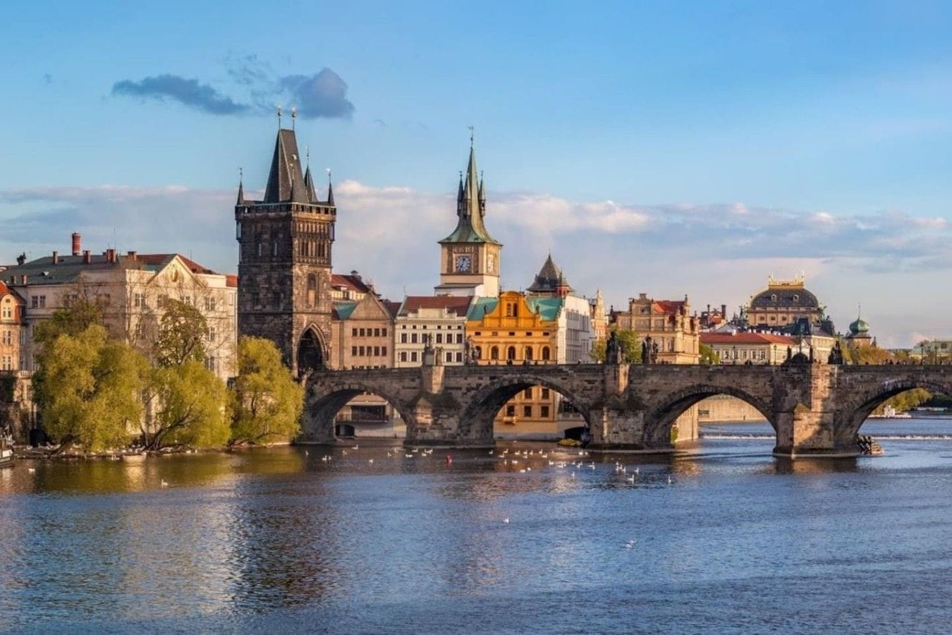 A historic bridge with multiple arches spanning a river, surrounded by buildings with varied architectural styles.