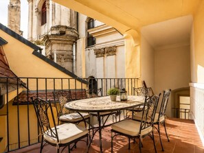 Ein runder Tisch mit Stühlen auf einem Balkon, mit Blick auf ein historisches Gebäude mit aufwendiger Architektur.