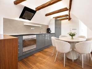 A modern kitchen with grey cabinets, stainless steel appliances, and a round dining table with chairs. - Old Prague Charm | Historic 2BR by Charles Bridge (Prague 1)