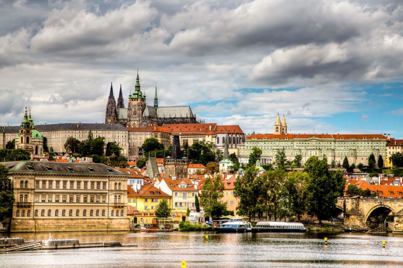 A historic cityscape with prominent architecture, including a cathedral and a castle, across a river.