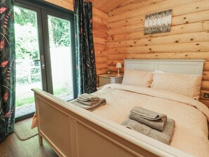 A wooden cabin bedroom with a bed, pillows, a nightstand, and a painting on the wall. - The Log Cabin (Ormskirk)