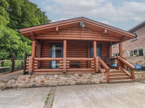 A log cabin with a stone foundation, a porch with wooden railings, and a chimney. - The Log Cabin (Ormskirk)