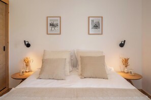 Ein Schlafzimmer mit einem Bett, zwei gerahmten Bildern an der Wand, zwei Nachttischen mit Lampen und einer Holztür.