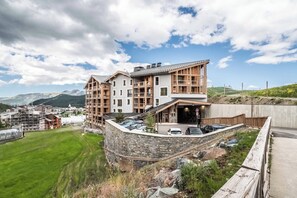 Un hôtel moderne doté d’un mur de soutènement en pierre, de nombreux balcons et offrant une vue sur les montagnes.