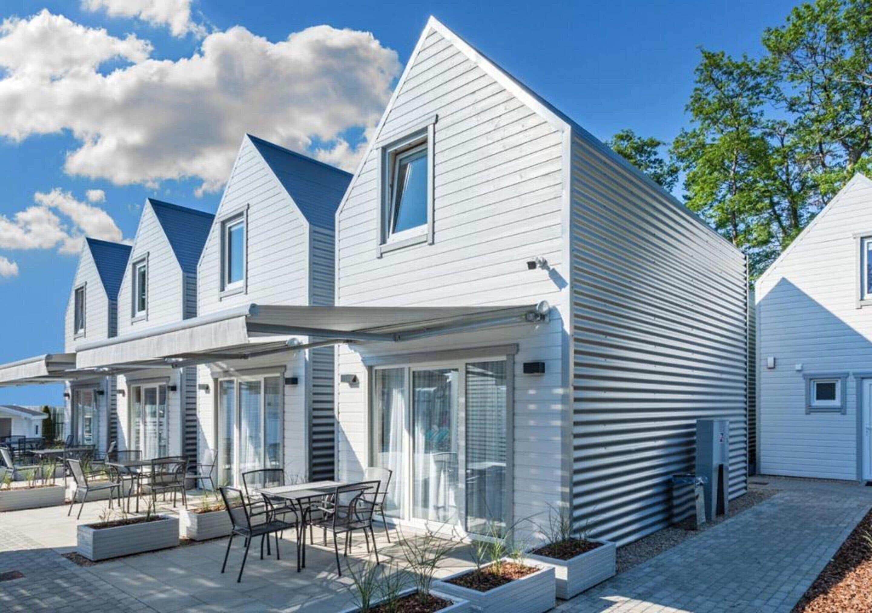 A modern residential building with a flat roof, large windows, and a covered patio area with outdoor furniture.