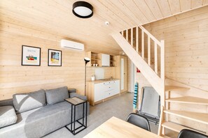 Ein kompakter Raum mit Holzboden, einem grauen Sofa, einem kleinen Tisch, einer Küchenzeile mit Schränken und einer Holztreppe.