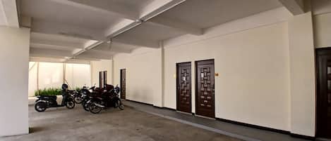 Un passadís amb una fila de portes tancades a un costat i motocicletes aparcades a l'altre.