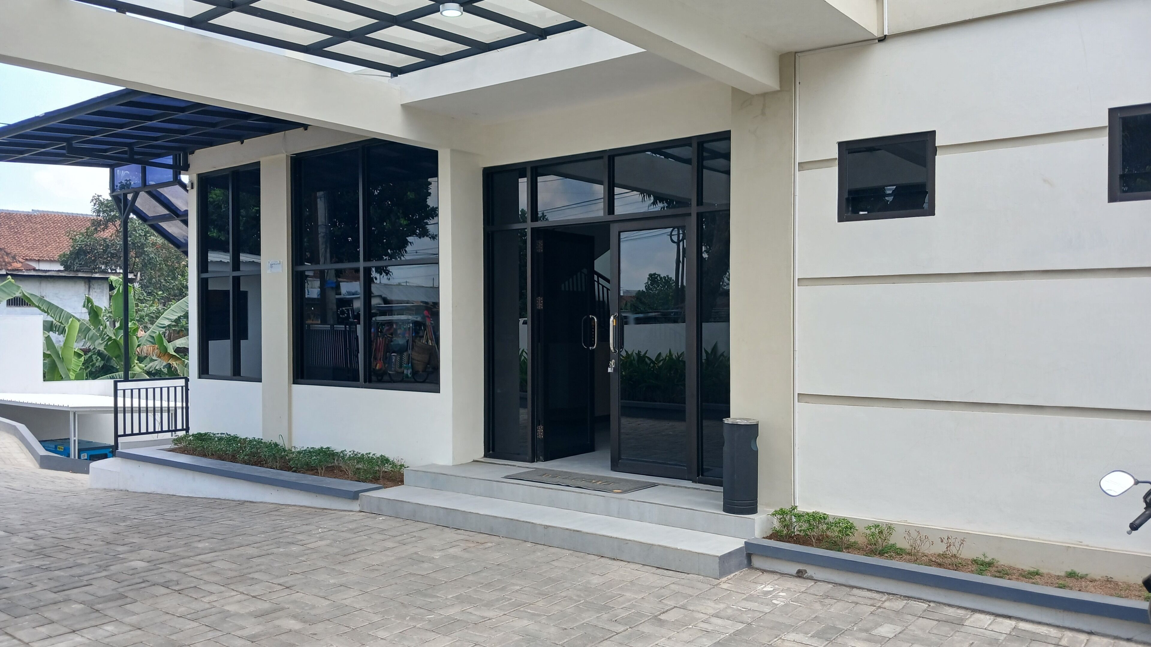 A modern building with a covered entrance, large windows, and a paved driveway.