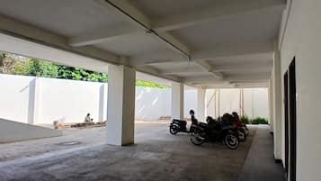 A covered outdoor area with concrete flooring, white walls, and a row of parked motorcycles.