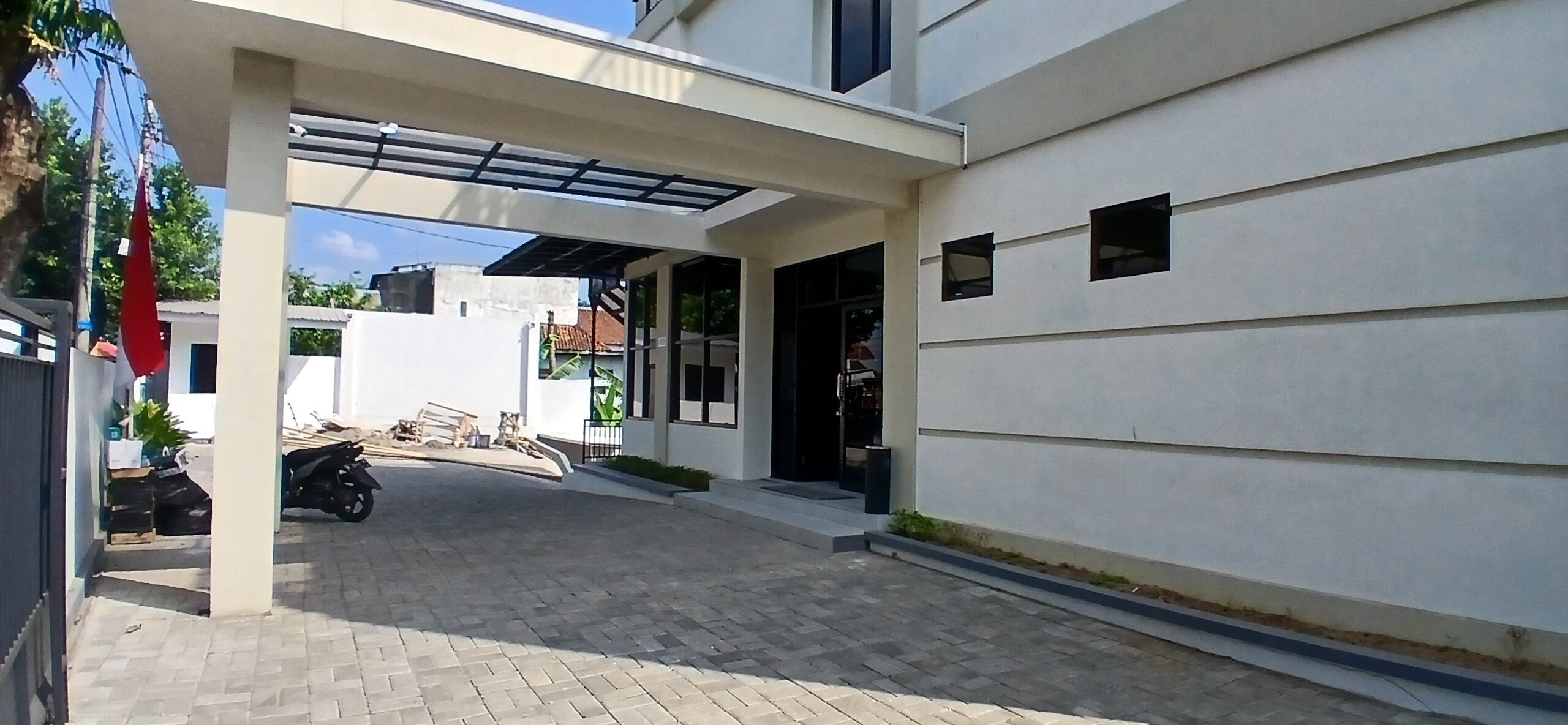Un edificio moderno con un acceso cubierto, un camino pavimentado y una moto estacionada.