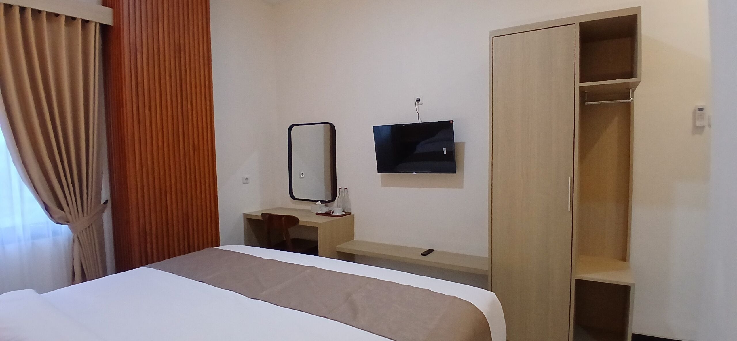 Une chambre d’hôtel comprenant un lit, un bureau, un miroir, une télévision et une armoire.