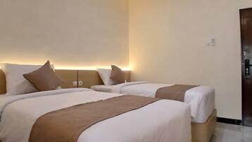 A hotel room with two beds, each with white and brown bedding, a wooden door, and a wall-mounted light fixture.