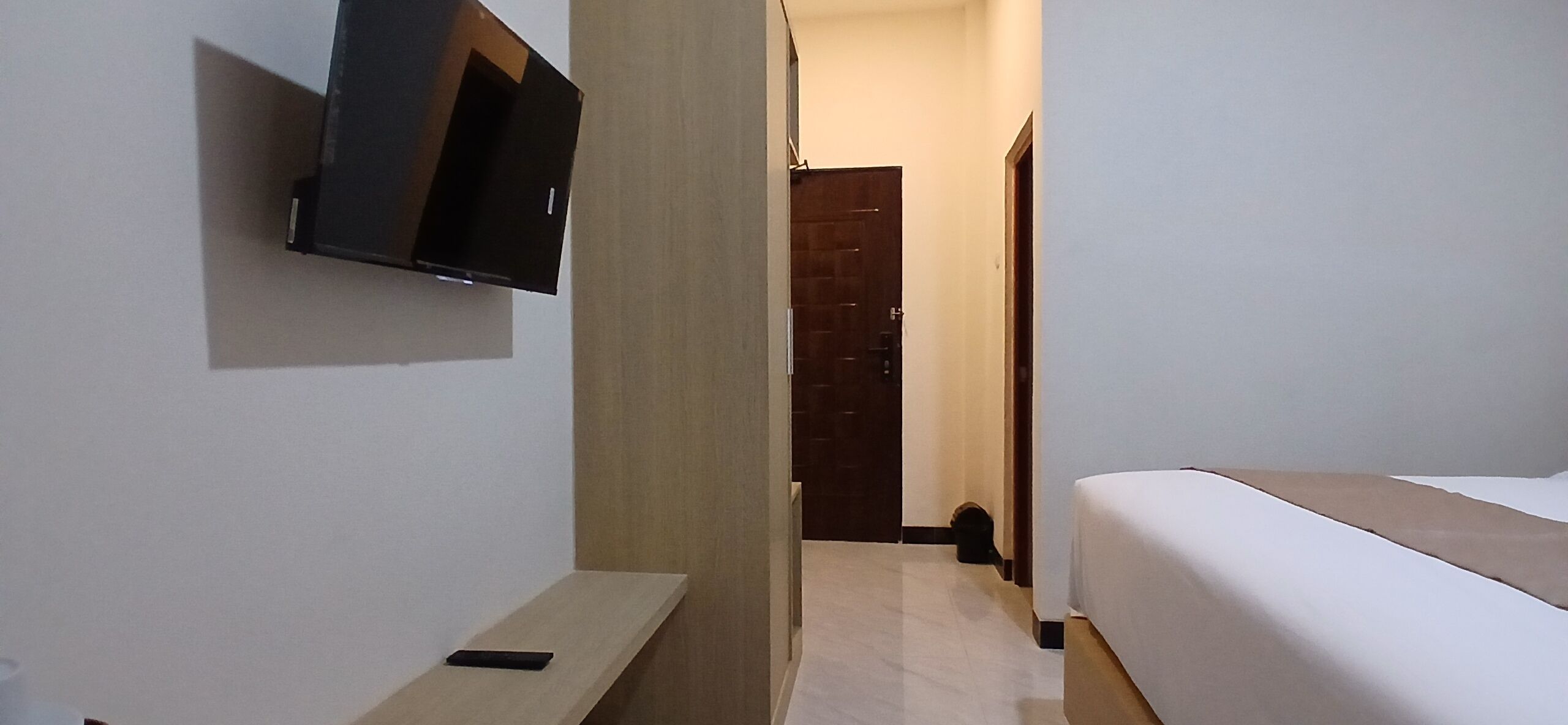 A hotel room with a bed, a TV mounted on the wall, a wooden door, and a small table.