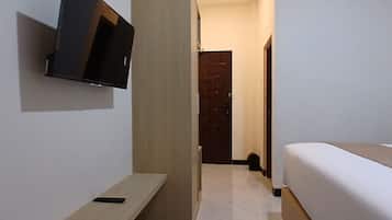 A hotel room with a bed, a TV mounted on the wall, a wooden door, and a small table.