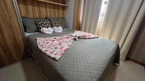 A bed with a quilted grey bedspread, two pillows with a floral pattern, and a folded blanket. - Apto 201 Flat Prático Perto de Tudo (Belém)