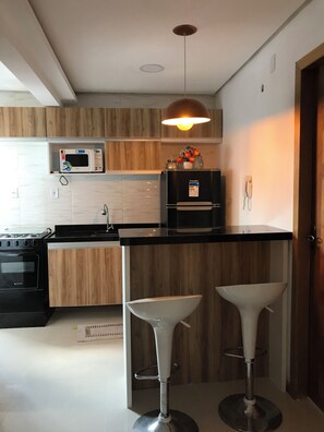 A modern kitchen with a microwave, stove, and refrigerator. There are two bar stools and a hanging light fixture. - Apto 201 Flat Prático Perto de Tudo (Belém)