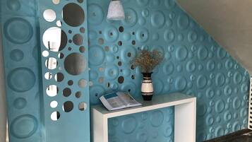 A reception area with a blue textured wall, a white console table, a vase with dried flowers, and a hanging light fixture.