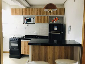 Una cocina con mostrador negro, armarios de madera, microondas, refrigerador y estufa.