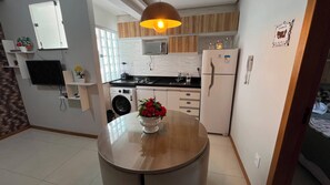 A compact kitchen with a washing machine, a refrigerator, and a dining area with a table. - Apto 201 Flat Prático Perto de Tudo (Belém)