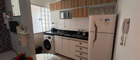 A compact kitchen with a microwave, refrigerator, sink, and a washing machine.