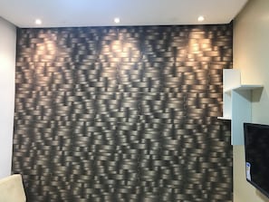 A room with a textured wall, recessed ceiling lights, a flat-screen TV, and a light-colored sofa.