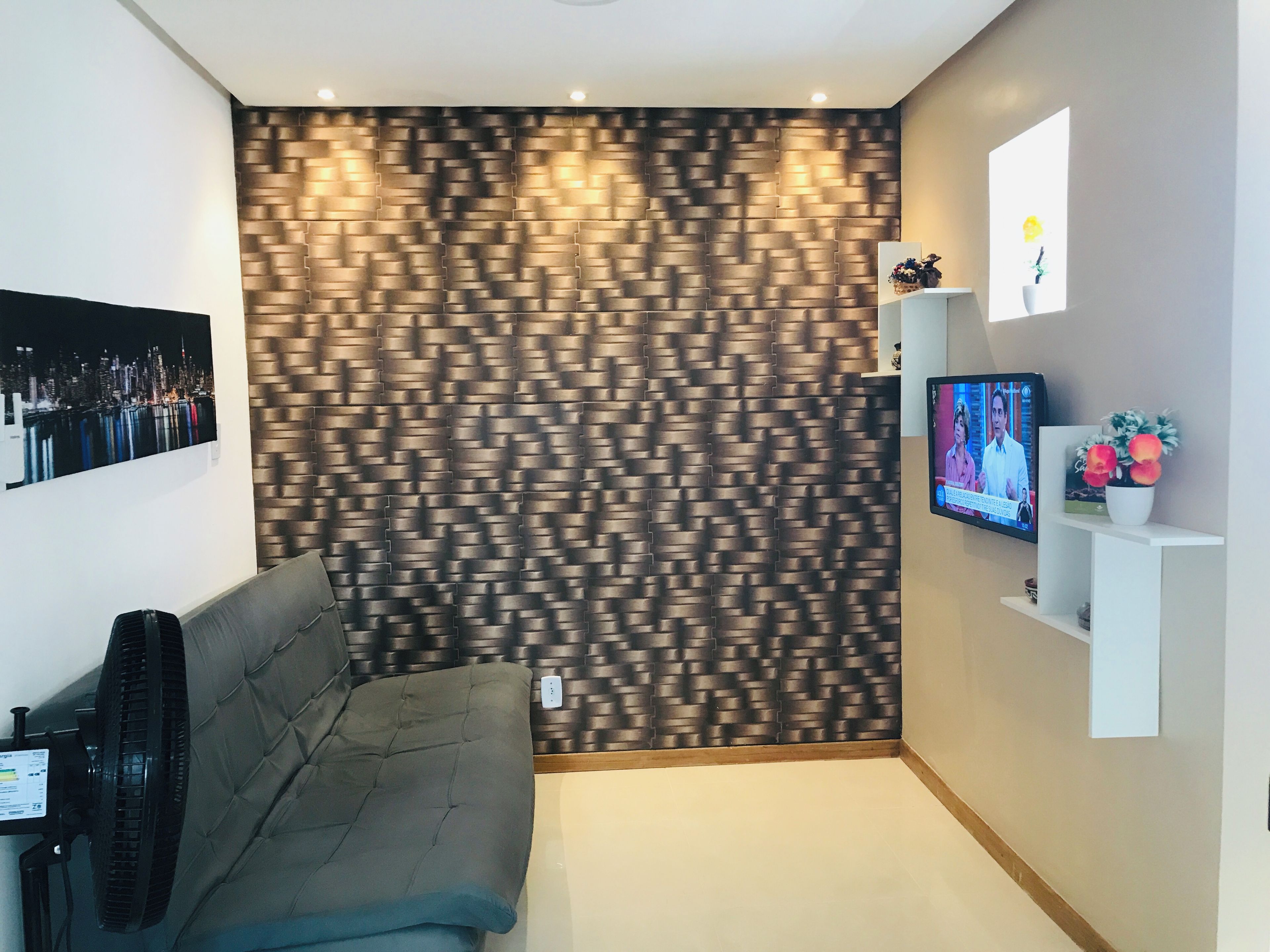 Una sala moderna con pared estampada, televisor de pantalla plana, sofá y una pequeña estantería blanca con objetos decorativos.