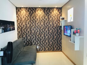 Una sala moderna con pared estampada, televisor de pantalla plana, sofá y una pequeña estantería blanca con objetos decorativos.