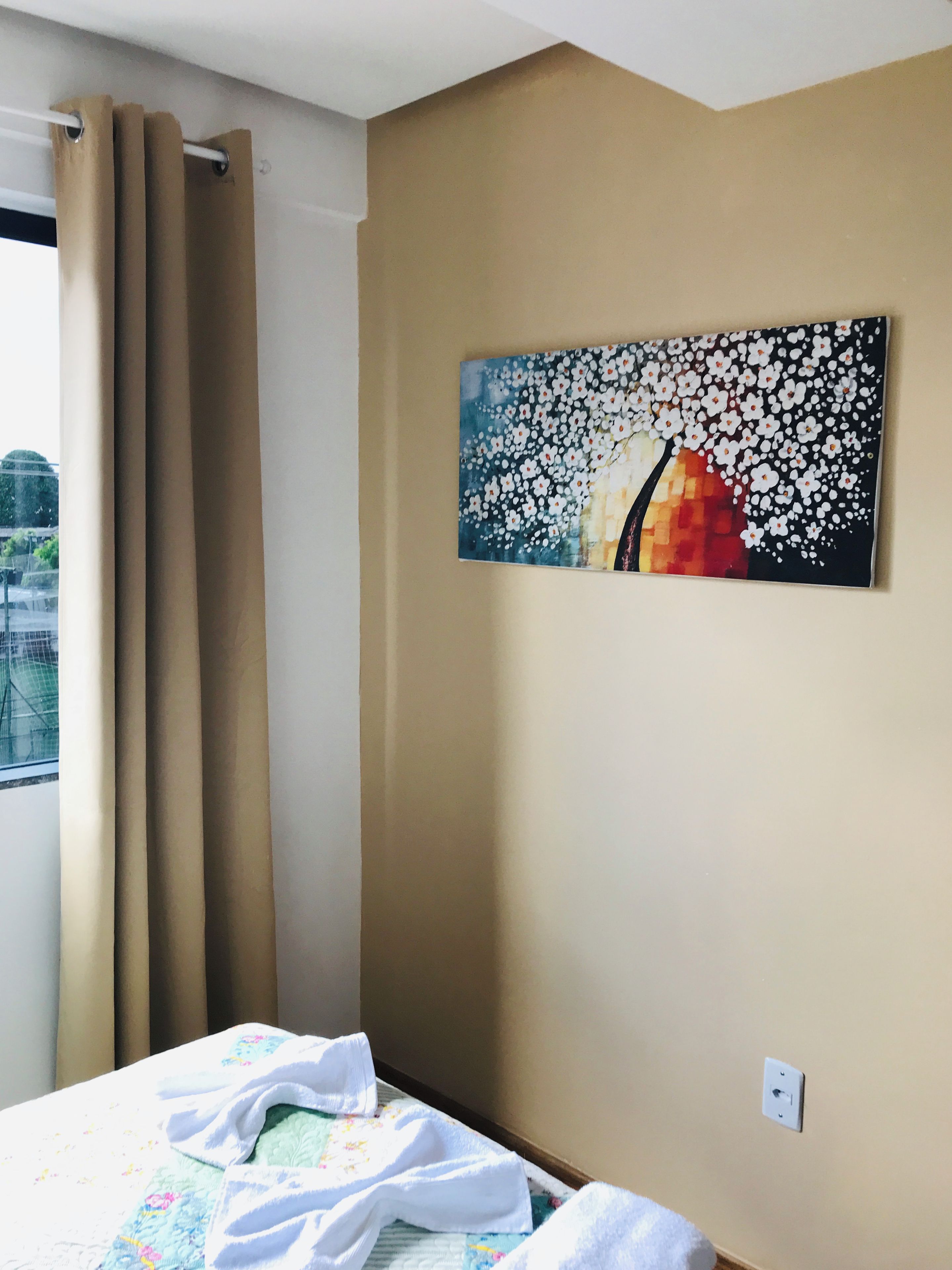 Habitación de hotel con cama, ventana con cortinas y un cuadro colgado en la pared.