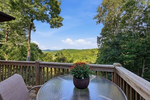 A glass-top table with a potted plant on a wooden deck overlooking a forested landscape.