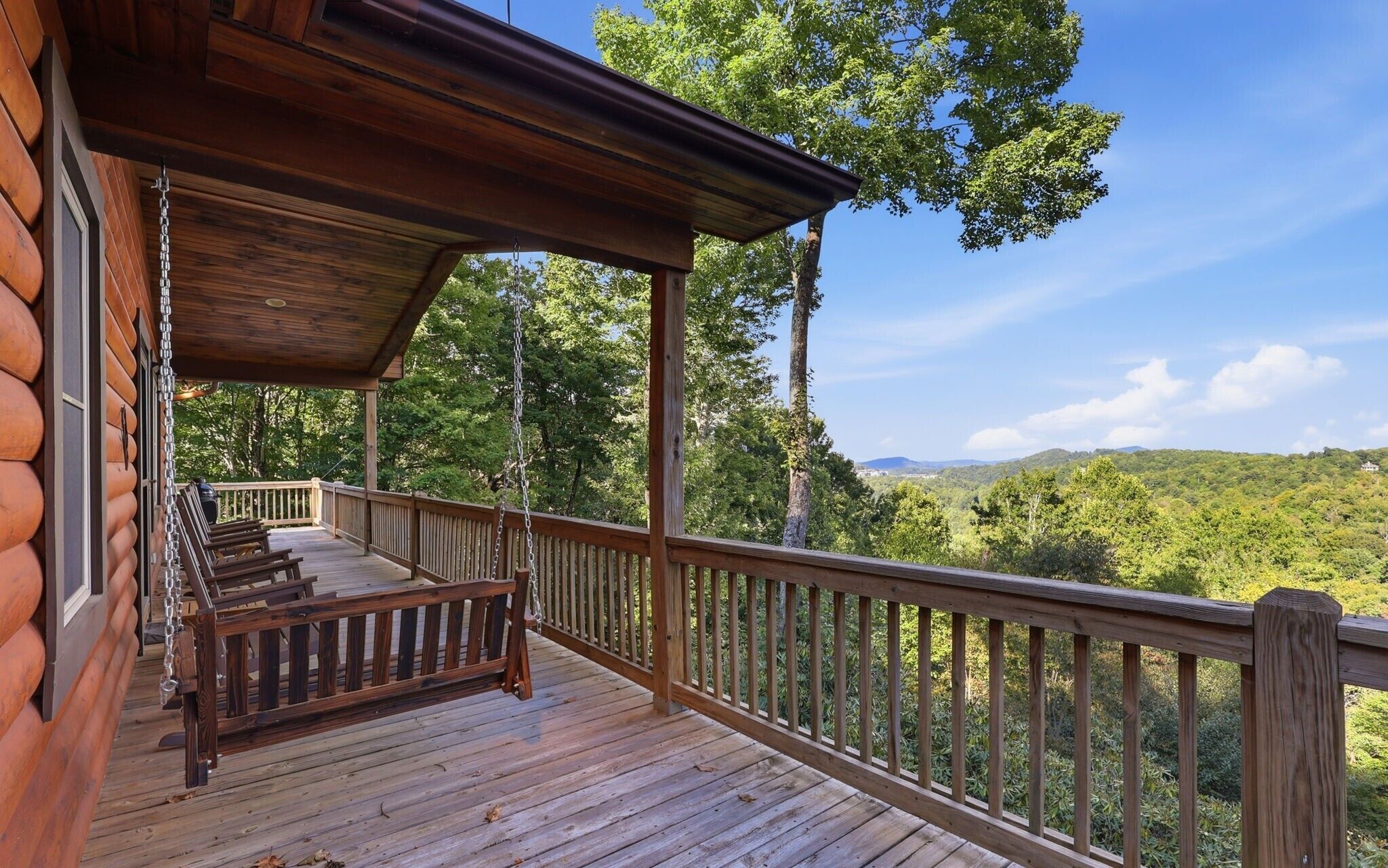 A wooden deck with a swing chair and a view of a forested landscape.